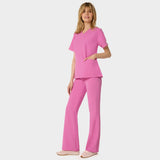 Bluza medyczna Emily w kolorze Disco Pink od Vena Uniformy.
Modelka stoi na jasnym tle w komplecie medycznym: bluza z krótkim rękawem oraz spodnie flare, zestawione z beżowymi sneakersami.