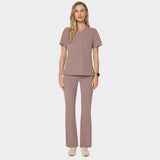 Bluza medyczna Emily w kolorze LIGHT BROWN od Vena Uniformy.
Modelka stoi na jasnym tle w  komplecie medycznym: bluza z krótkim rękawem oraz spodnie flare, zestawione z beżowymi sneakersami.