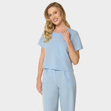 Bluza medyczna Gaja crop w kolorze BABY BLUE od Vena Uniformy.
Modelka stoi na jasnym tle w pastelowym komplecie medycznym: bluza z krótkim rękawem oraz szerokie spodnie.