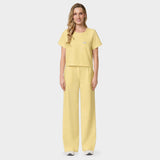 Spodnie medyczne damskie Aura w kolorze BUTTER YELLOW od Vena Uniformy.
Modelka stoi na jasnym tle w pastelowym komplecie medycznym: bluza z krótkim rękawem oraz szerokie spodnie, zestawione z jasnymi sneakersami.