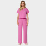 Bluza medyczna Gaja crop w kolorze Disco Pink od Vena Uniformy.
Modelka stoi na jasnym tle w komplecie medycznym: bluza z krótkim rękawem oraz szerokie spodnie, zestawione z beżowymi sneakersami.