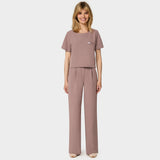 Bluza medyczna Gaja crop w kolorze LIGHT BROWN od Vena Uniformy.
Modelka stoi na jasnym tle w  komplecie medycznym: bluza z krótkim rękawem oraz szerokie spodnie, zestawione z beżowymi sneakersami.