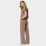 Bluza medyczna Gaja crop w kolorze MOCHA od Vena Uniformy.
Modelka stoi na jasnym tle w  komplecie medycznym: bluza z krótkim rękawem oraz szerokie spodnie, zestawione z beżowymi sneakersami.