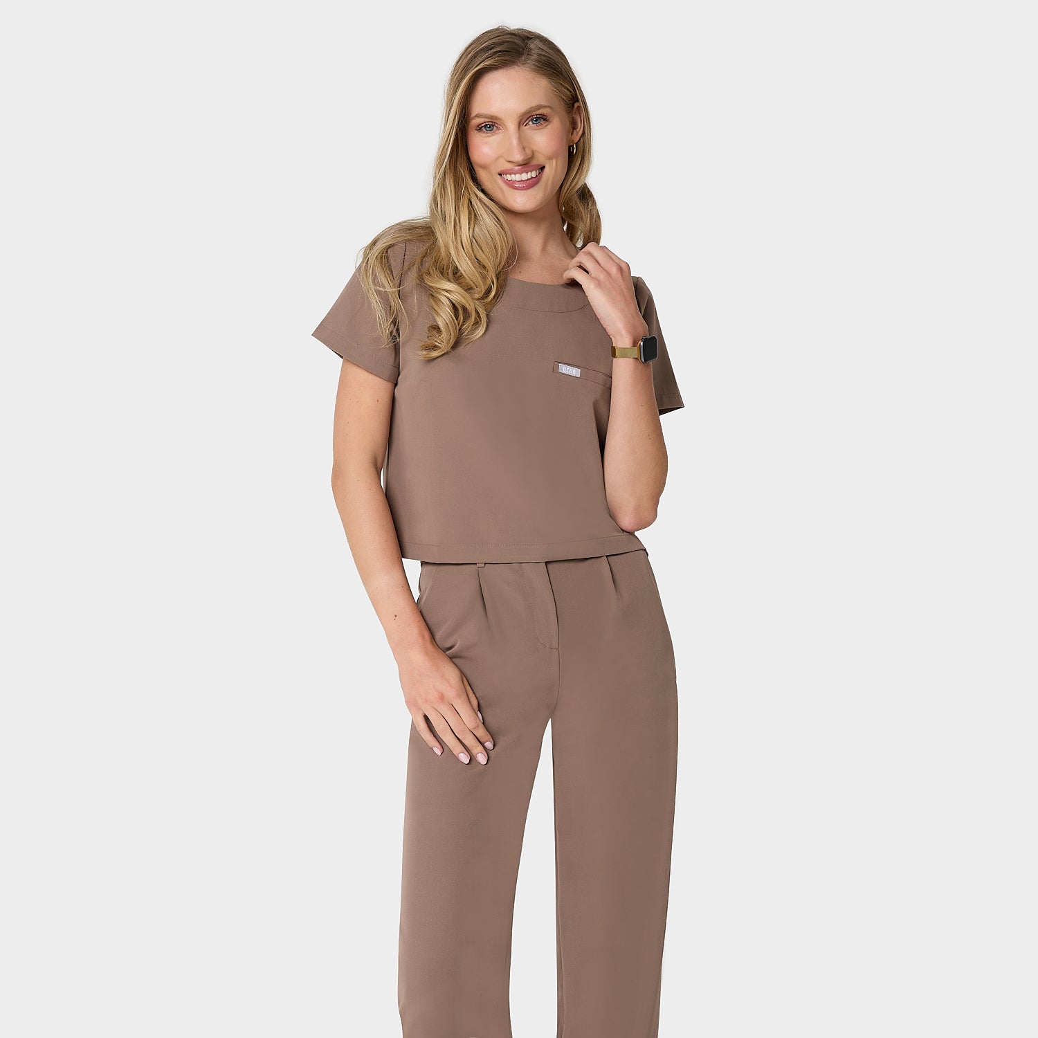 Bluza medyczna Gaja crop w kolorze MOCHA od Vena Uniformy.
Modelka stoi na jasnym tle w komplecie medycznym: bluza z krótkim rękawem oraz szerokie spodnie.