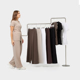 Damskie spodnie medyczne Aura LATTE w różnych kolorach wiszące na wieszakach, w towarzystwie modelki.