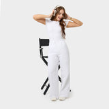 Damskie spodnie medyczne Aura WHITE, szerokie nogawki, wysoka talia, wygodne, modne, eleganckie, modelka w słuchawkach.