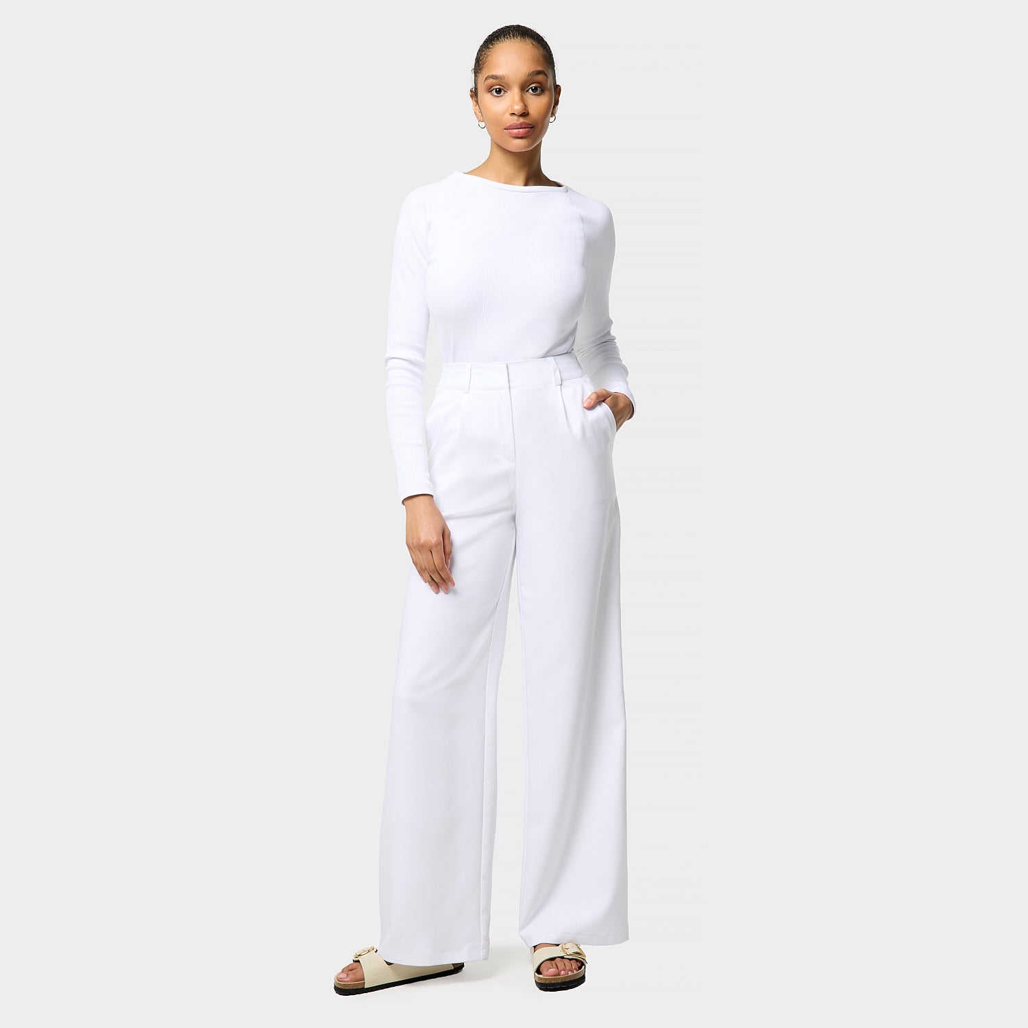 Damskie spodnie medyczne Aura WHITE o szerokich nogawkach, z wysoką talią, na modelce w białej bluzce longsleeve.